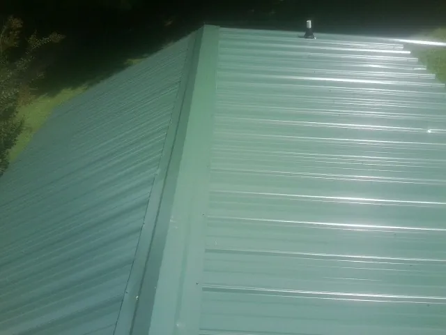 New green metal panels meeting at the ridge of a roof — Flat Roof Repair work by our crew in Mason