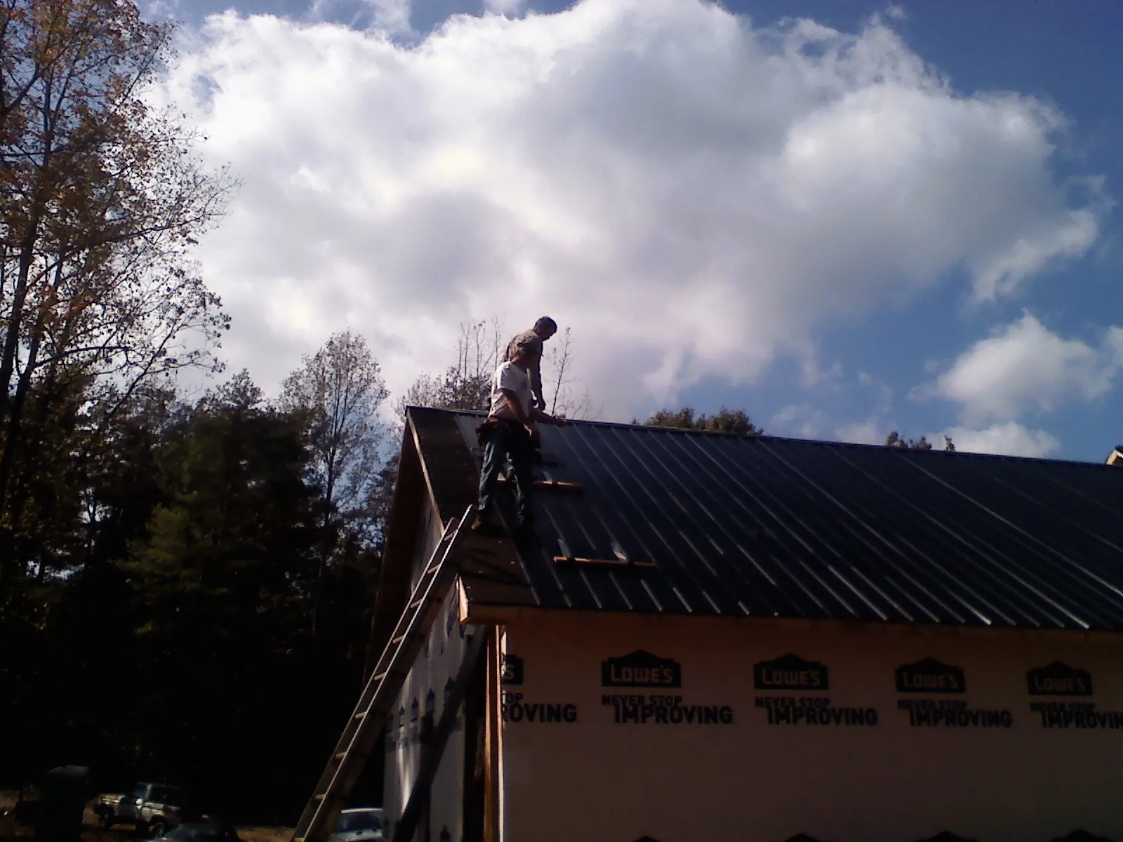 Roofer fastening dark metal panels high against a cloudy sky, from a Roof Inspection job in Mason